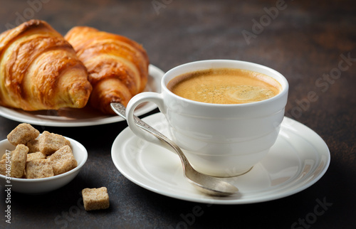 Cup of fresh coffee with croissants on dark background.