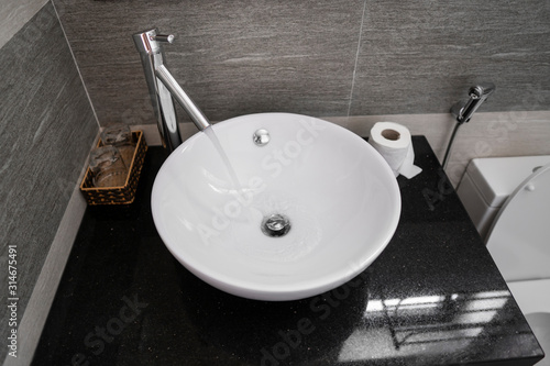 Bathroom interior with white round sink and chrome faucet in a modern bathroom. Water flowing from the chrome faucet.