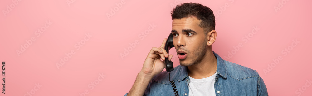 Panoramic shot of shocked man with telephone handset looking away isolated on pink Panoramic shot of shocked man with telephone handset looking away isolated on pink