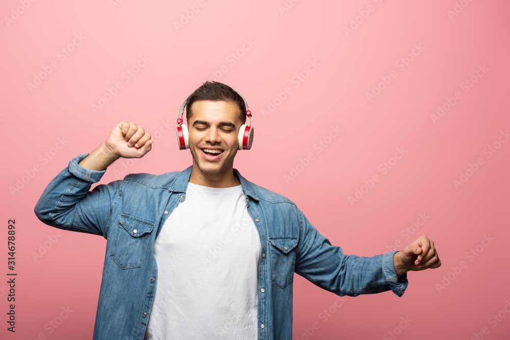 Smiling man with closed eyes dancing while using headphones isolated on pink Smiling man with closed eyes dancing while using headphones isolated on pink