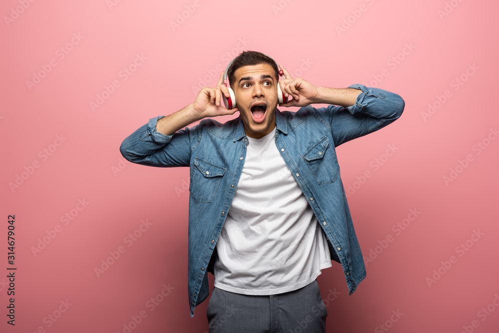 Shocked man in headphones looking away on pink background Shocked man in headphones looking away on pink background