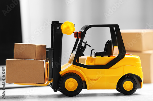 Toy forklift with boxes near laptop on table. Logistics and wholesale concept