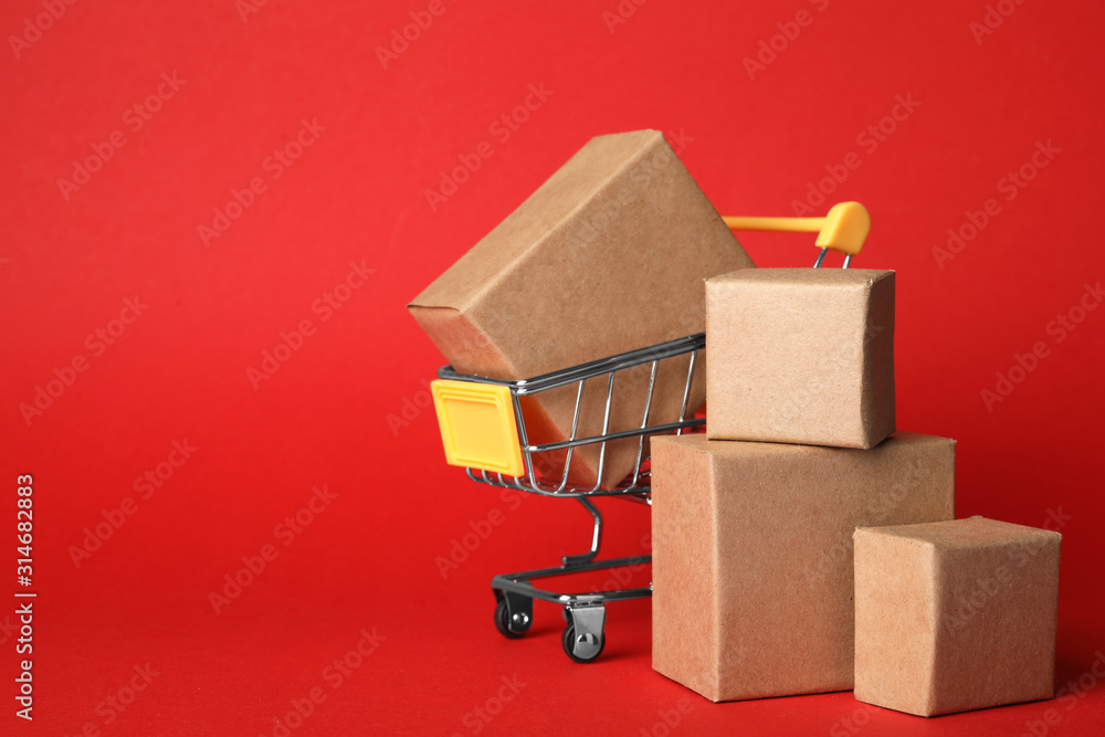 Shopping cart and boxes on red background, space for text. Logistics and wholesale concept - obrazy, fototapety, plakaty 