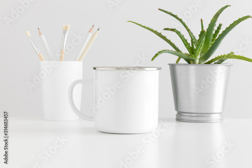 Enamel mug mockup with workspace accessories and a succulent plant on a white table. photo