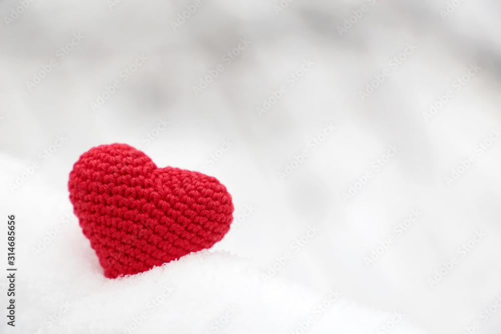 Obraz premium Valentine heart in winter forest. Red knitted heart, symbol of romantic love in the snow, concept of Valentines day
