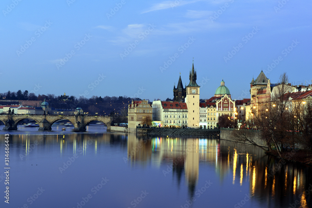 Urban scene with old Town Bridge Tower, clock tower and St. Francis Of Assisi Church in Prague, Czech Republic while sunset