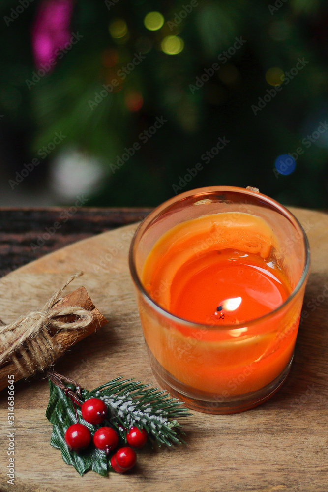 Beautiful Christmas orange mandarin candle on a wooden stand with sticks of whole cinnamon, sprig of mistletoe and a Christmas tree decorated with toys. Christmas New year evening mood, greeting card