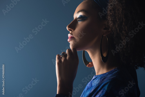 side view of attractive african american woman with accessories isolated on blue