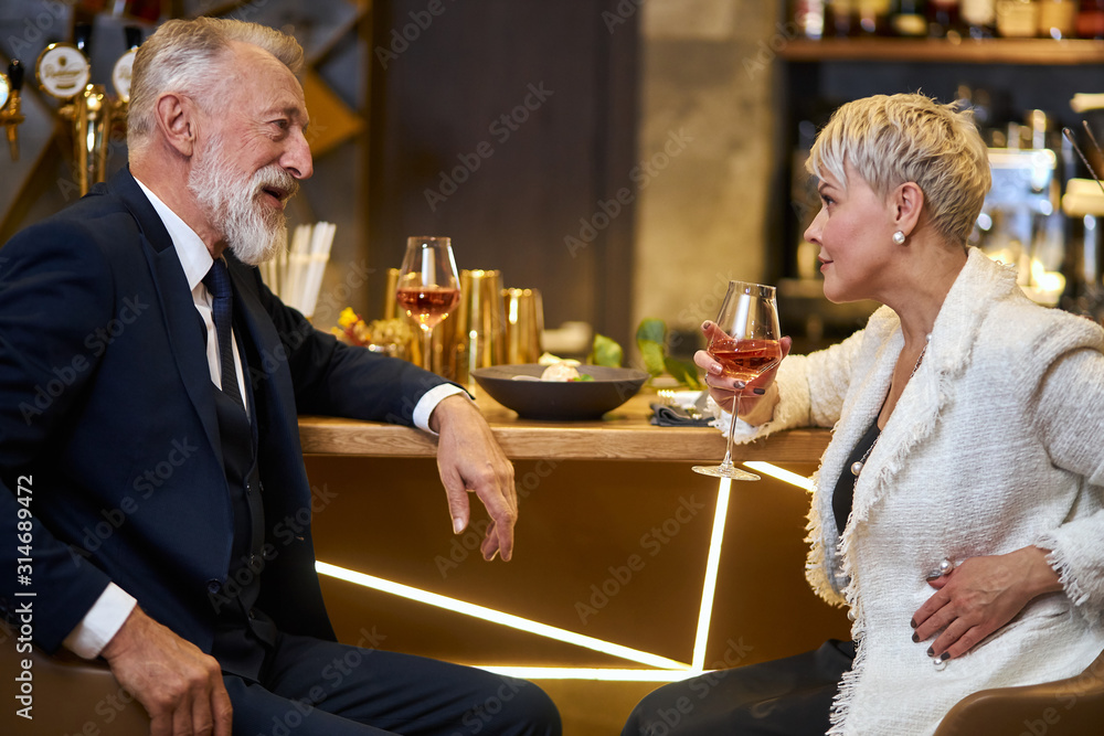 Caucasian man in tuxedo and woman in white blazer have conversation, smile and happy together in love. Background elegant expensive restaurant
