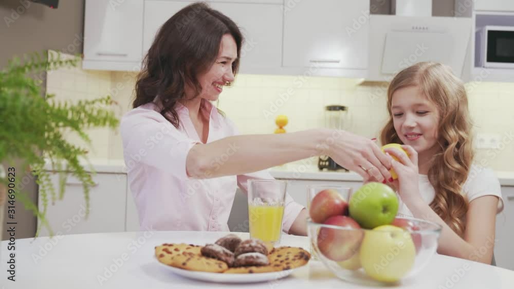 Little girl and charming woman sitting at table in kitchen Little girl and charming woman sitting at table in kitchen