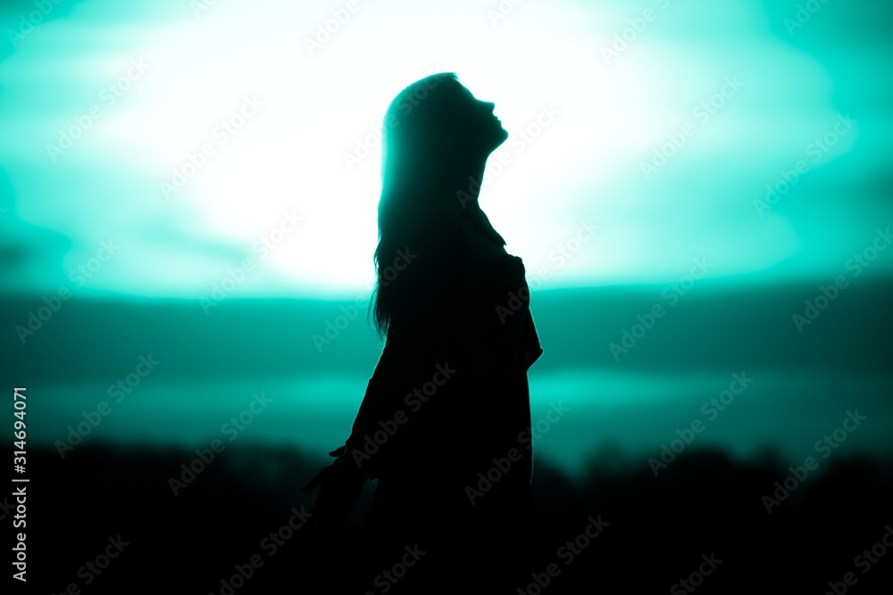 Youth woman soul turquoise sun meditation awaiting future times. Silhouette in front of sunset or sunrise in summer nature. Symbol for healing burnout therapy, wellness relaxation or resurrection