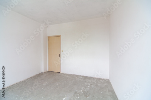 Closed wooden door in empty room, white walls. New empty room under construction. Interior renovation.