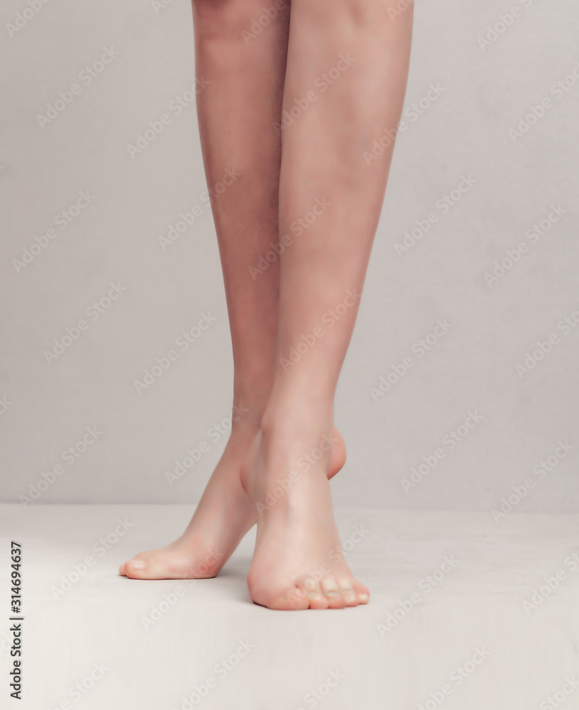 Slender female legs raised on toes on a light gray background