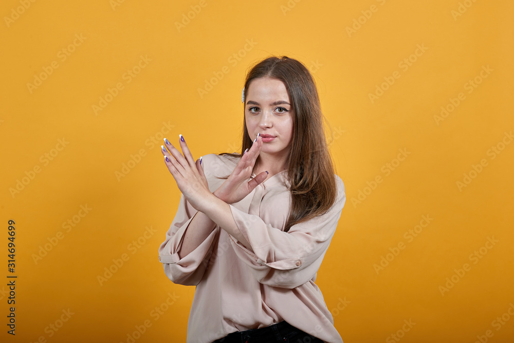 Disappointed caucasian woman in fashion pastel shirt staying sideways, crossed hands, stop gesture isolated on orange background in studio. People sincere emotions, lifestyle concept. Disappointed caucasian woman in fashion pastel shirt staying sideways, crossed hands, stop gesture isolated on orange background in studio. People sincere emotions, lifestyle concept.