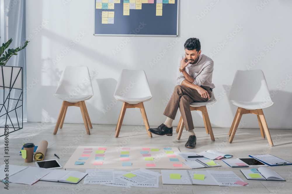 Fototapeta premium pensive mixed race businessman sitting on chair near sticky notes