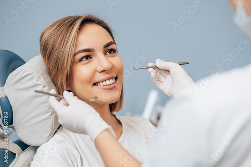 attractive woman with short hair sit in dental office and look at doctor with confidence, she has perfect smile. professional doctor of clinic use special sterilized medical instruments