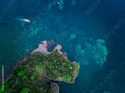 Aerial view of a steep cliff and a motor boat. Jagged coast on the Adriatic Sea. Cliffs overlooking the transparent sea. Wild nature and Mediterranean maquis