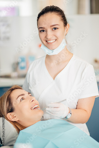 portrait of female dentist in white doctor's uniform standing in office near equipment and look at camera. Medicine, dentist, orthodontic concept