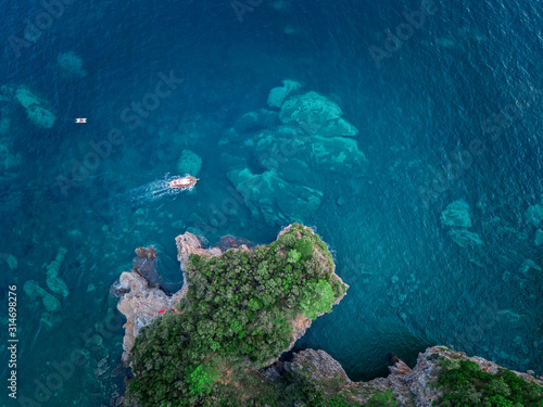 Aerial view of a steep cliff and a motor boat. Jagged coast on the Adriatic Sea. Cliffs overlooking the transparent sea. Wild nature and Mediterranean maquis