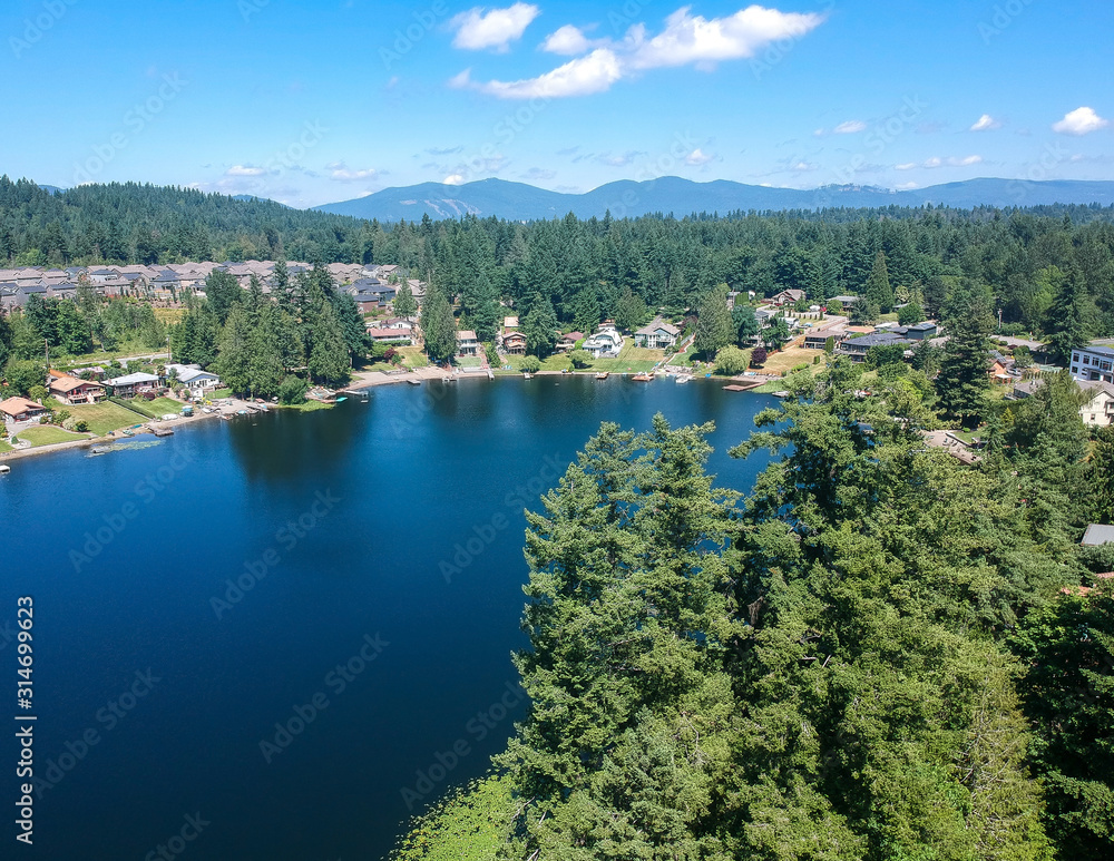Obraz premium Tranquil Shady Lake on a bright clear day in summertime with trees reflecting in the water a blue sky and white clouds with lily pads dockside in Renton King County Washington State