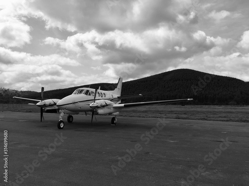 Black and white photographed plane parked in isolated airport with mountain in the background