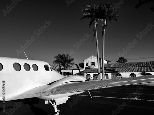 Black and white photographed plane parked in abandoned airport with trees in the background