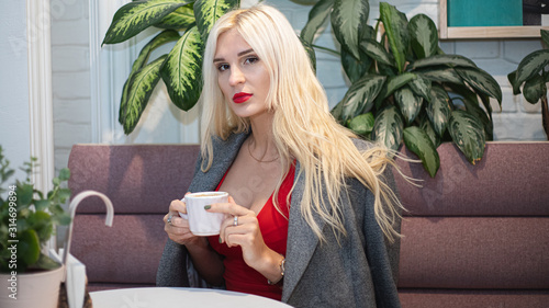 Young beautiful blond woman in an autumn coat seets in the cafe. Soft focus. Fashionable concept. photo