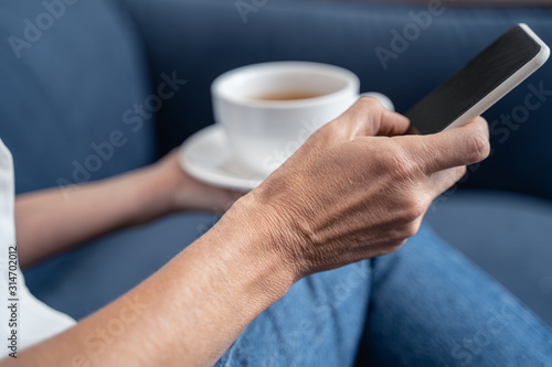 Hands holding a cellphone and tea cup