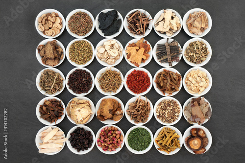 Fotografie Traditional Chinese herb collection used in herbal medicine in white porcelain bowls on slate background