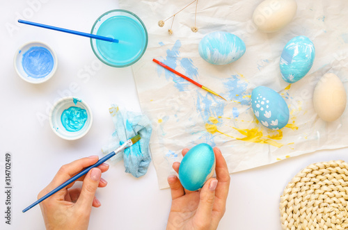 Flat lay girl painting Easter eggs with blue Paints. Hold paint brush and paints traditional easter pattern on a wooden egg