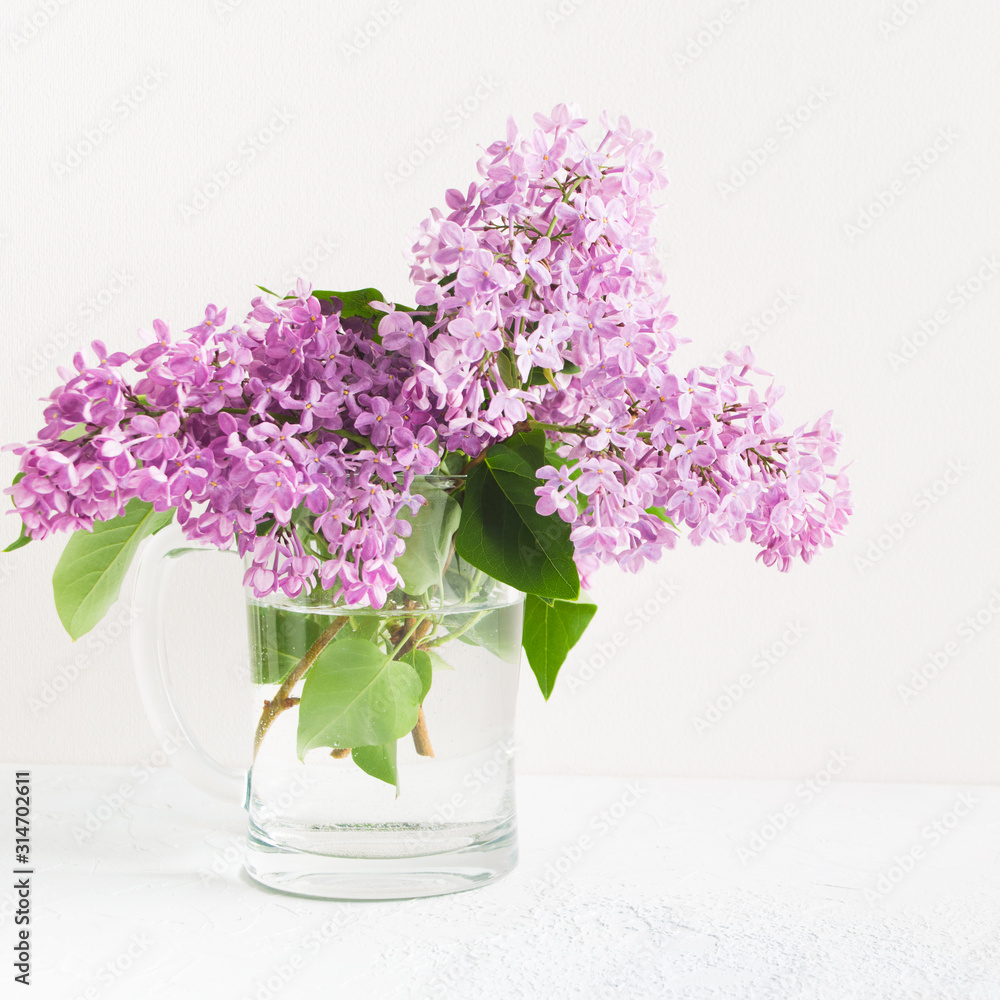 Obraz premium Branches of fresh purple lilac in glass vase
