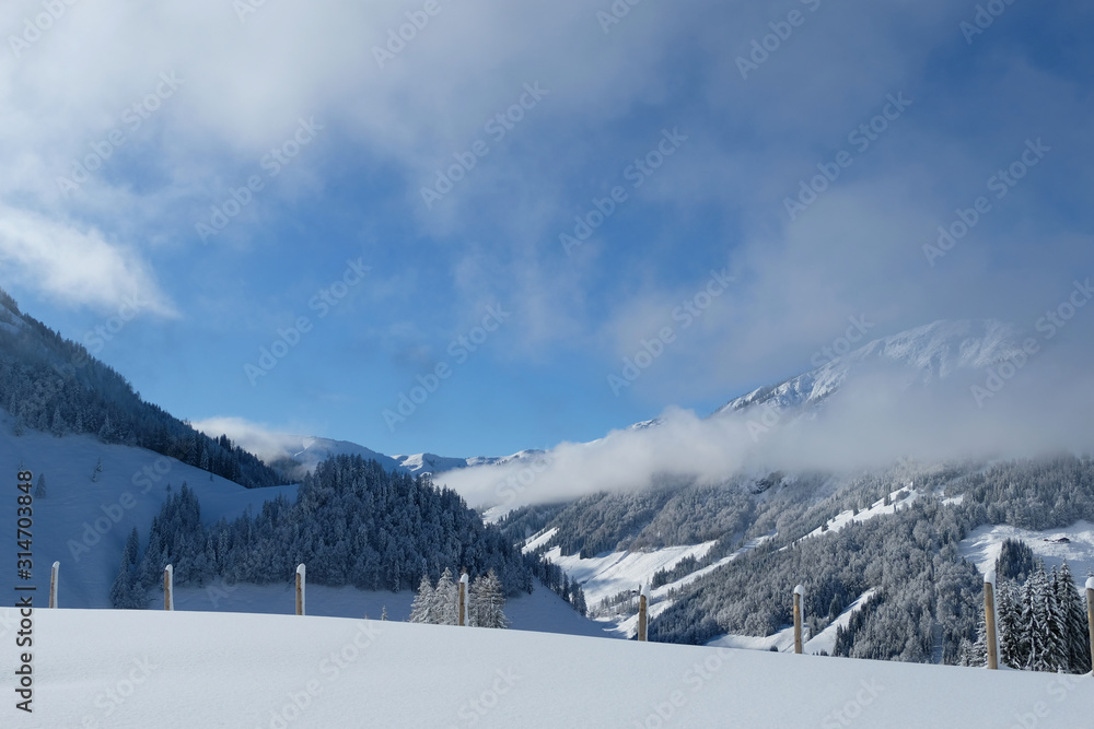 Beautiful panorama of snow covered Kitzbuehleler Horn, Austrian alps mountain peak. Low clouds hang around the mountain ranges and over the valley. Glittering shiny deep fresh powder snow foreground.