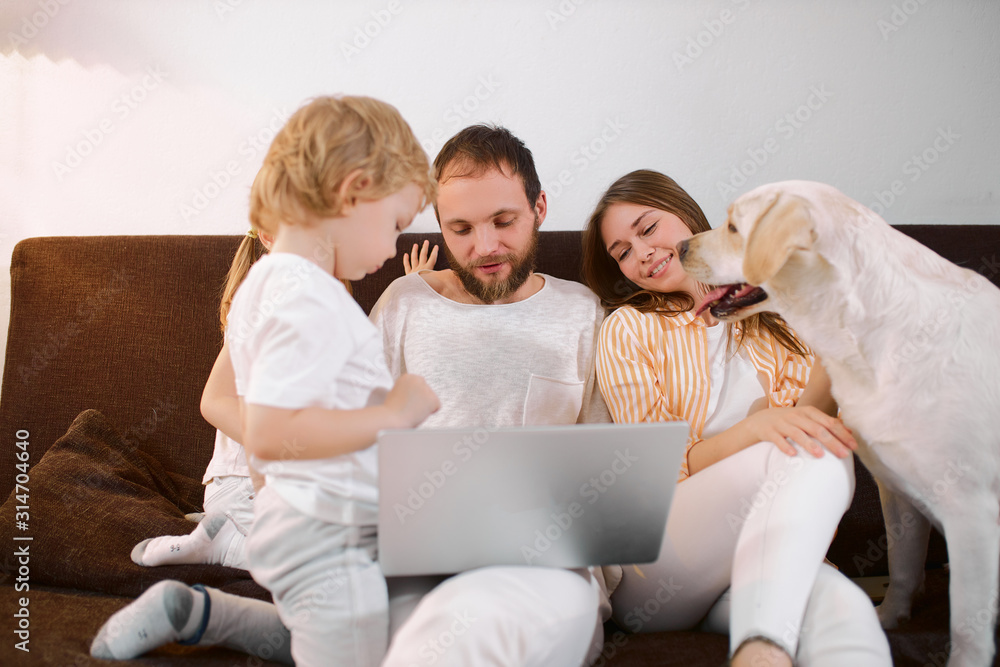 happy caucasian family resting at home together with children, friendly pet dog, using modern laptop, wearing white casual clothes happy caucasian family resting at home together with children, friendly pet dog, using modern laptop, wearing white casual clothes