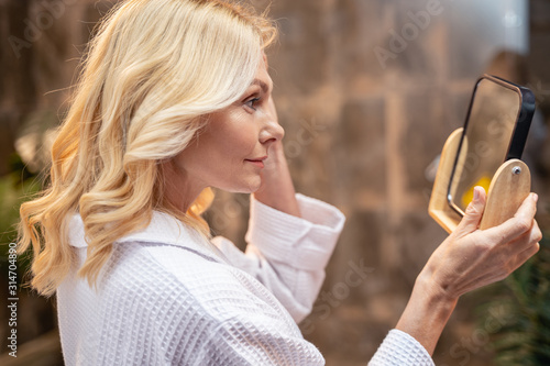 Focused calm Caucasian female examining her face