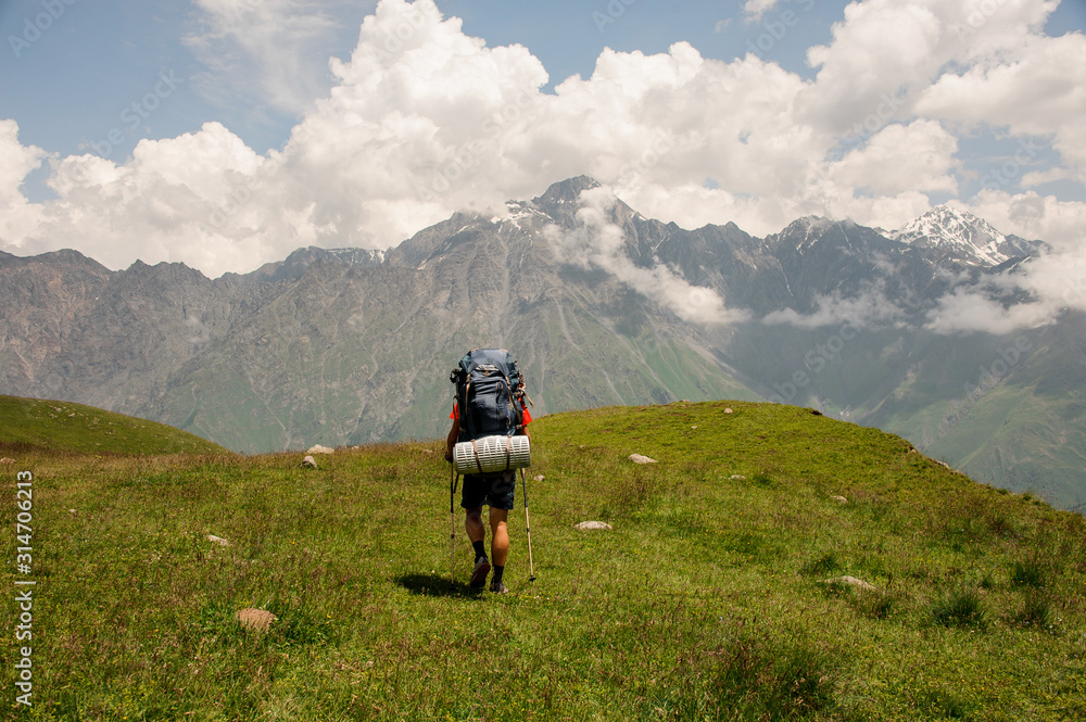 Hiker with backpack walks among hills and mountains