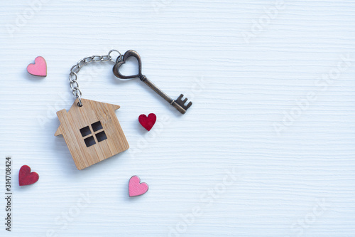 House key in heart shape with home keyring on old wood background decorated with mini heart