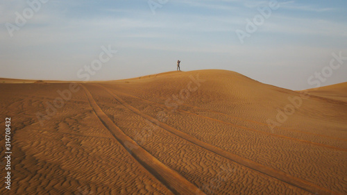 desert landscape with traces of the car in the foreground and the figure of the photographer in the distance, Dubai, UAE
