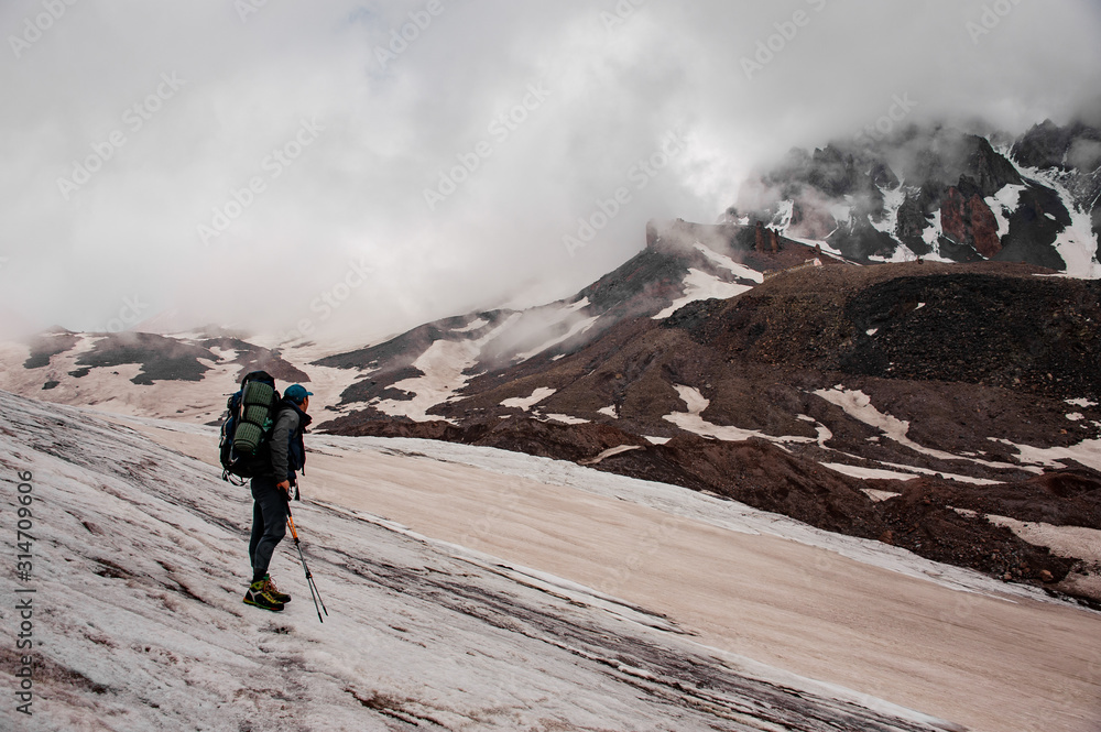 Tourist with backpack and sticks looks at mountain