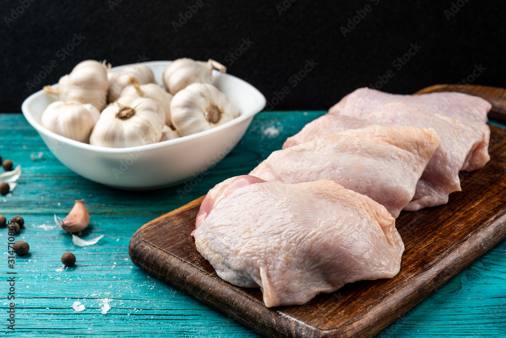Fototapeta premium Raw chicken thighs on blue wooden background.