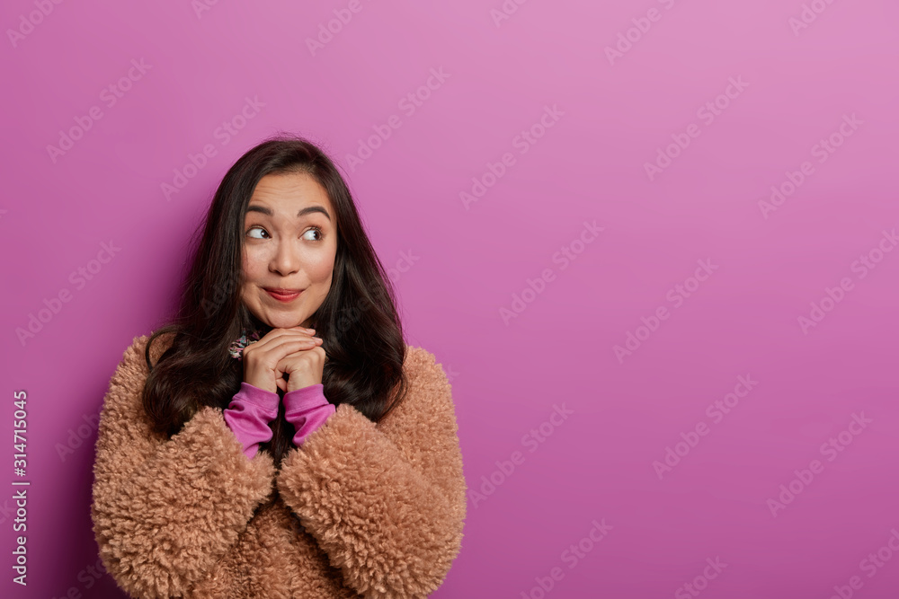 Photo of lovely Korean woman keeps gaze aside, hands under chin, has long straight hair, thinks about something, has pleasant memories, isolated on lilac background. Human facial expressions Photo of lovely Korean woman keeps gaze aside, hands under chin, has long straight hair, thinks about something, has pleasant memories, isolated on lilac background. Human facial expressions