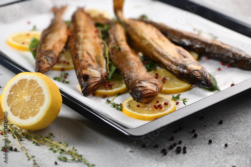 Whole fish, fried or smoked, on a baking sheet with lemon and herbs. photo