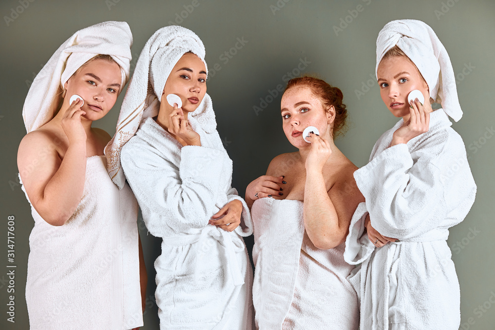 Attractive women with natural beauty use cotton pads after shower, stand in towels and bathrobes. Isolated over grey background. Skin care concept Attractive women with natural beauty use cotton pads after shower, stand in towels and bathrobes. Isolated over grey background. Skin care concept