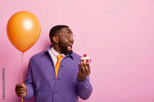 Canvas Print Cheerful shocked Afro American man stands with party balloon and sweet dessert, cannot believe eyes to see former lover on birthday dressed elegantly has pleasant wonder