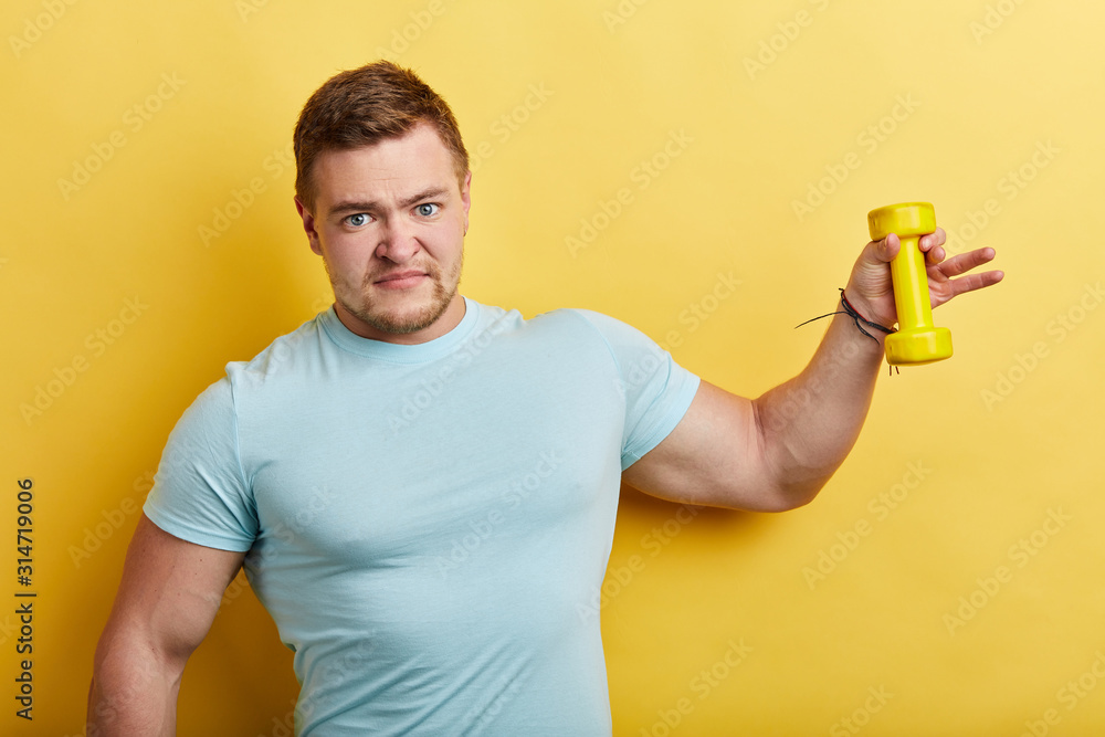 young serious muscular man lifting dumbbell.Isolated on yellow background, close up portrait, studio shot.man doesn't want to work out with dumbbell, guy isn't satisfied with training young serious muscular man lifting dumbbell.Isolated on yellow background, close up portrait, studio shot.man doesn't want to work out with dumbbell, guy isn't satisfied with training
