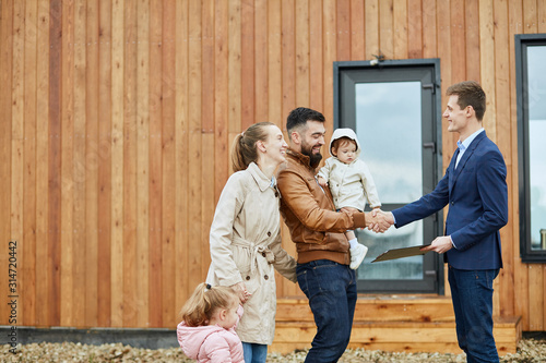 Fotografie Caucasian happy family of four and realtor wear blue suit stand outdoor near new house just sold