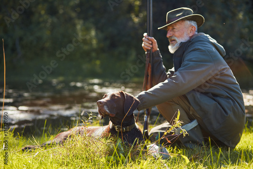 Obraz na plátně Obedient hunter dog sit with his owner near forest lake after hunting on wild ducks