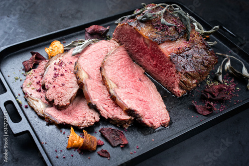 Traditional Commonwealth Sunday roast with sliced cold cuts roast beef with vegetable chips and herbs as closeup on a modern design tray