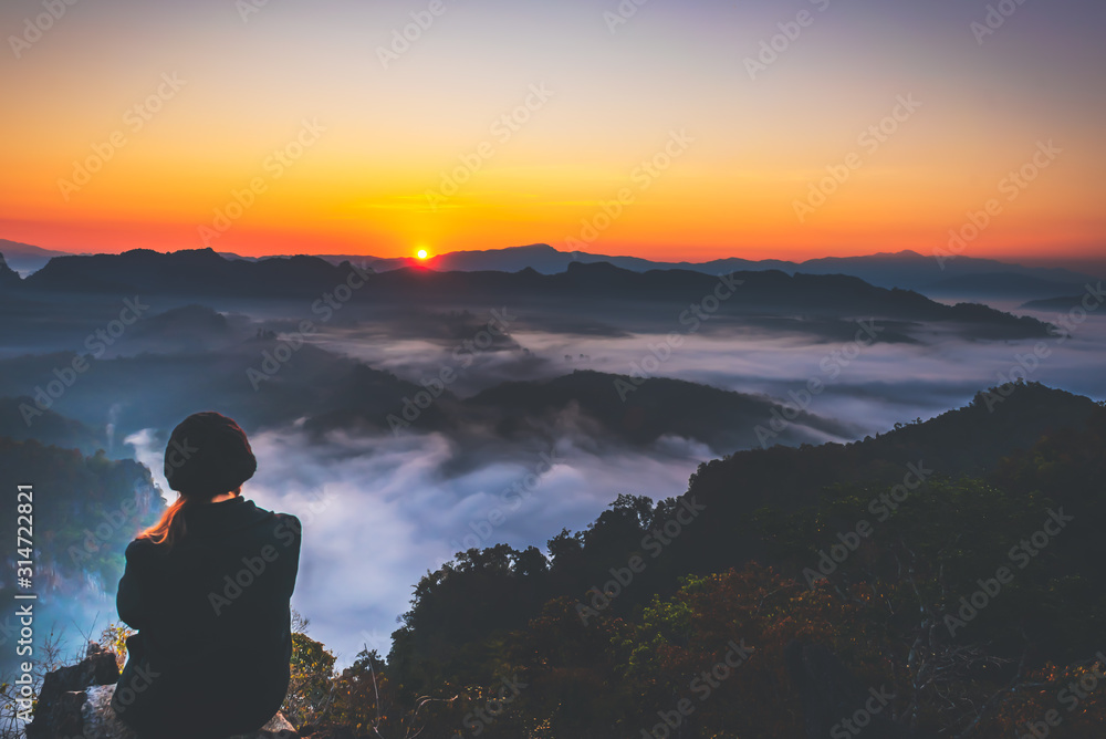 Lanscape images and the back of female tourist Sitting on a high mountain Looking at the rising sun behind the hill And white mist That covers the mountains to travel on vacation concept.