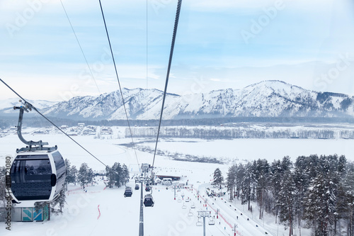 Landscape in Altay mountains with a gondola cableway booths suspended on a cable with skis and snowboards with snow on winter sunset. Ski resorts and snowboarding.