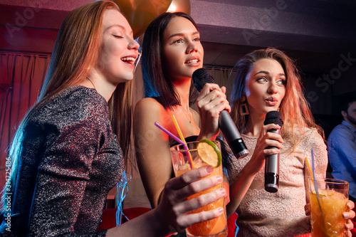 good-looking ladies and guys have leisure time in karaoke bar, dancing, having fun together in karaoke club, drinking and eating